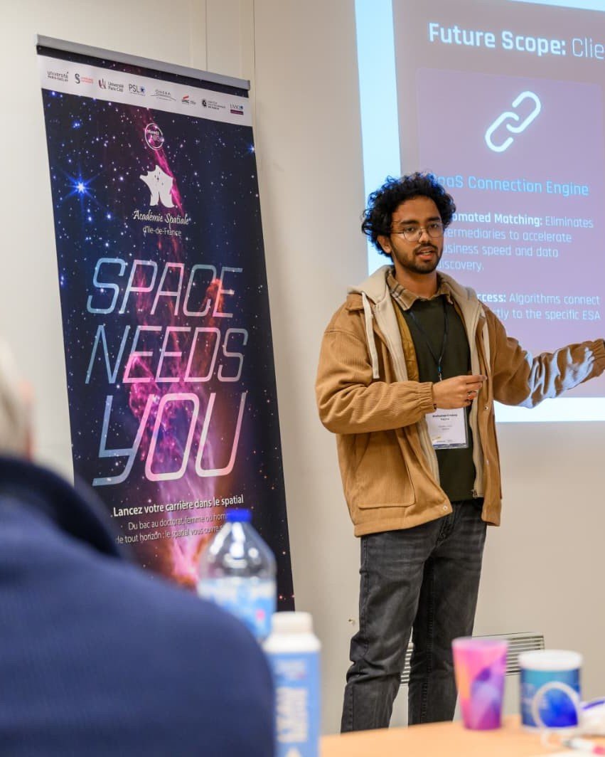 Anshuman pitching at Académie Spatiale Île-de-France, a "space needs you" banner beside him.